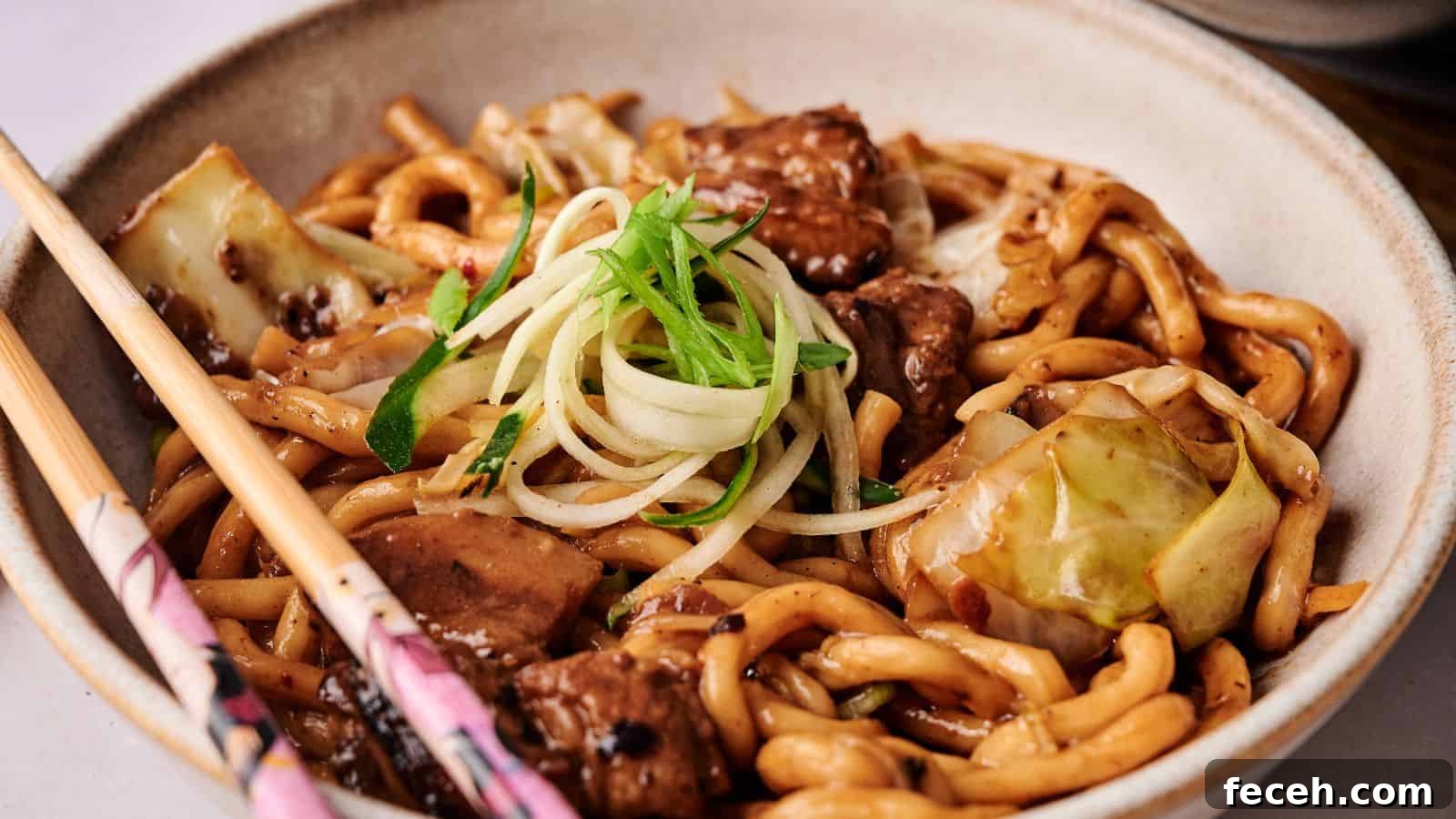31 Asian Weeknight Dinners to Make Mealtime Exciting 16 A bowl of stir-fried udon noodles with beef, cabbage, and green onion garnish, served with a pair of chopsticks on the side.