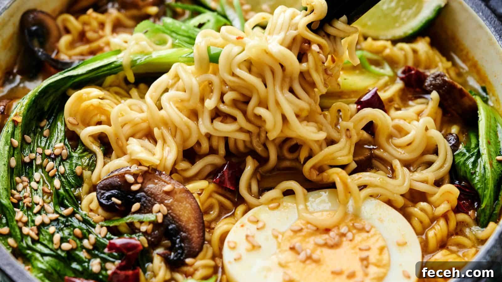31 Asian Weeknight Dinners to Make Mealtime Exciting 18 Close-up of a bowl of ramen with noodles, bok choy, mushrooms, half a boiled egg, sesame seeds, and lime, garnished with chili slices. Black chopsticks hold some noodles above the bowl.