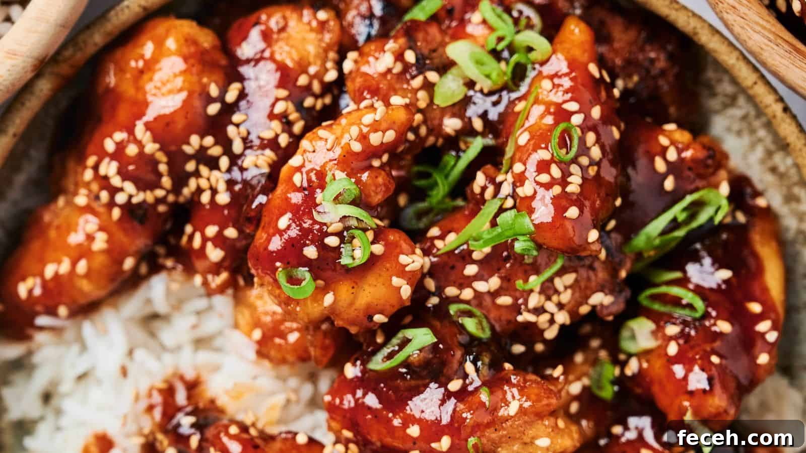 31 Asian Weeknight Dinners to Make Mealtime Exciting 21 A close-up of glazed chicken pieces with sesame seeds and chopped scallions on a bed of rice.