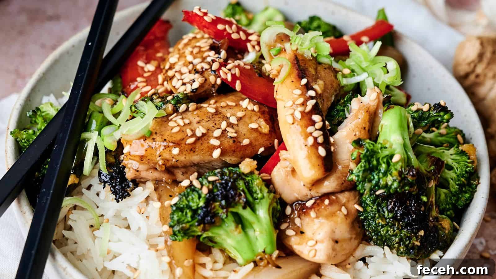 31 Asian Weeknight Dinners to Make Mealtime Exciting 23 A bowl of rice topped with broccoli, chicken, red peppers, green onions, and sesame seeds, with black chopsticks resting on the side.