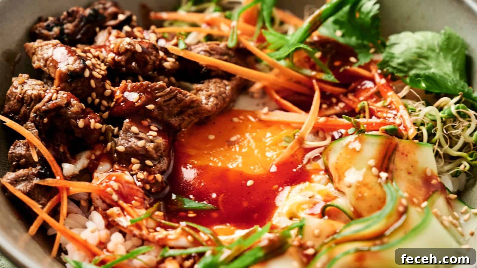 31 Asian Weeknight Dinners to Make Mealtime Exciting 24 A bowl of bibimbap with sliced beef, egg yolk, carrots, cucumber, greens, and bean sprouts, topped with sesame seeds and red sauce.