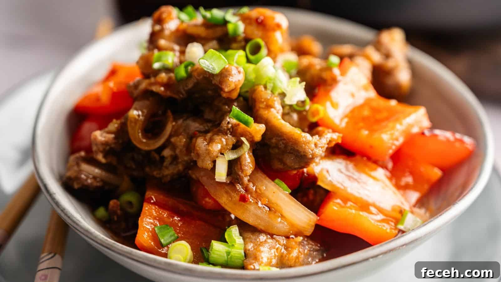 31 Asian Weeknight Dinners to Make Mealtime Exciting 33 A bowl of stir-fried beef with red bell peppers, onions, and chopped green onions, served on a white plate.