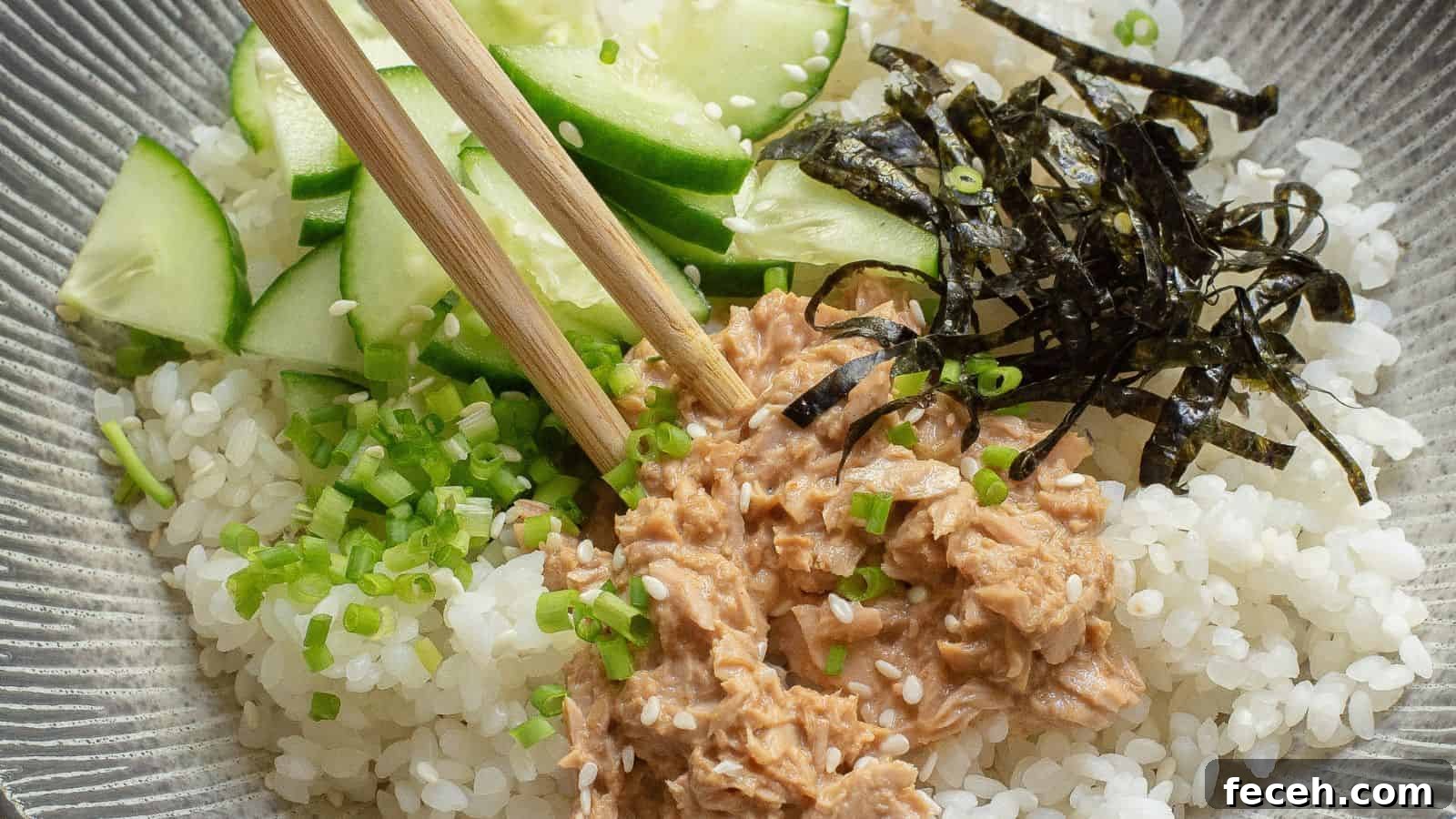 31 Asian Weeknight Dinners to Make Mealtime Exciting 5 A bowl of white rice topped with sliced cucumber, shredded nori, chopped green onions, and a portion of tuna, with a pair of chopsticks resting on top.