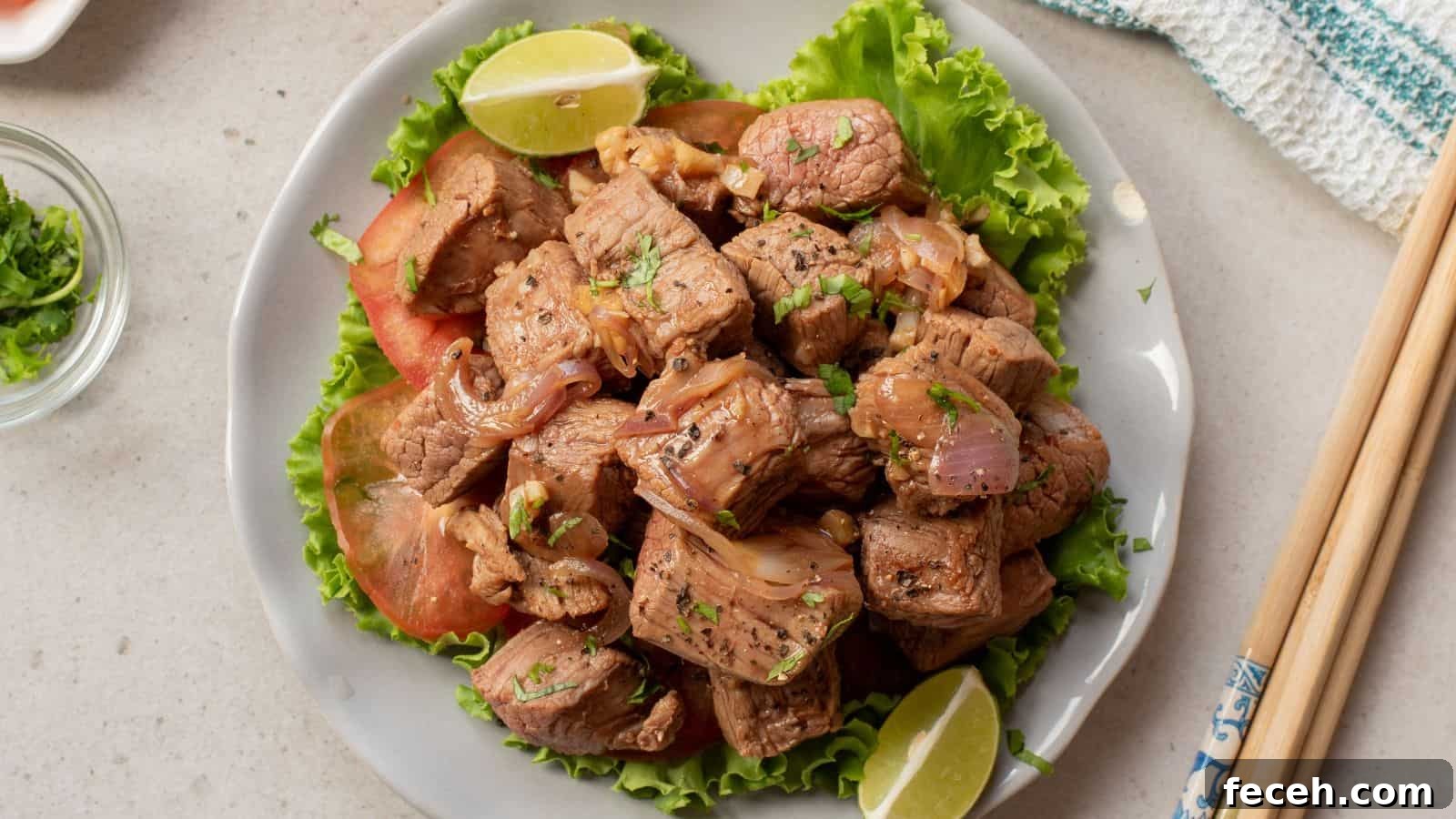 31 Asian Weeknight Dinners to Make Mealtime Exciting 9 A plate of stir-fried beef cubes with onions, garnished with cilantro, served on lettuce with tomato slices and lime wedges. Chopsticks rest beside the plate.