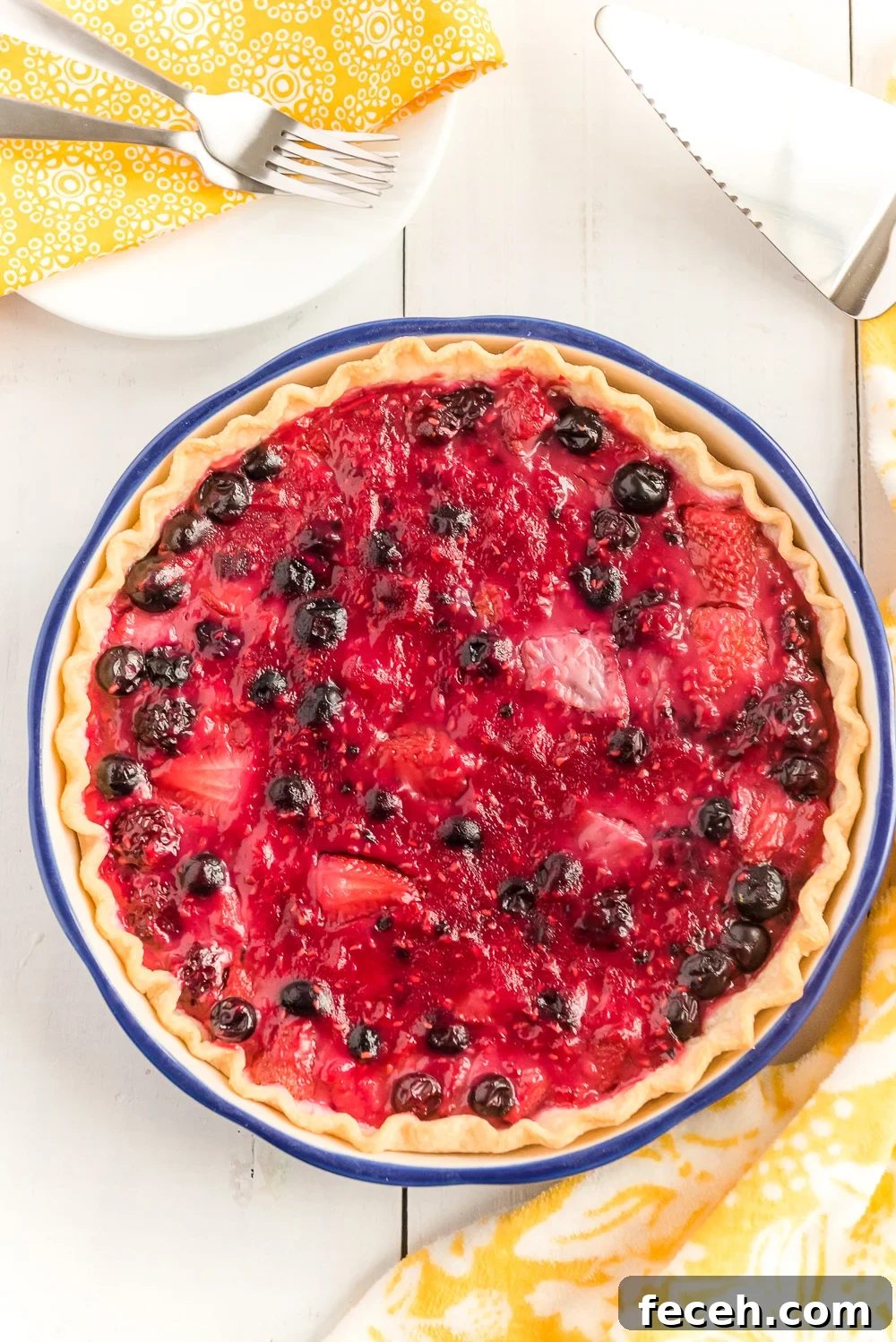 Overhead shot of a whole Mixed Berry Pie on white wood table.