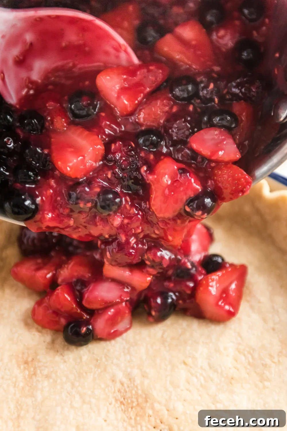 Mixed Berry Pie filling being poured into a prepared pie crust.