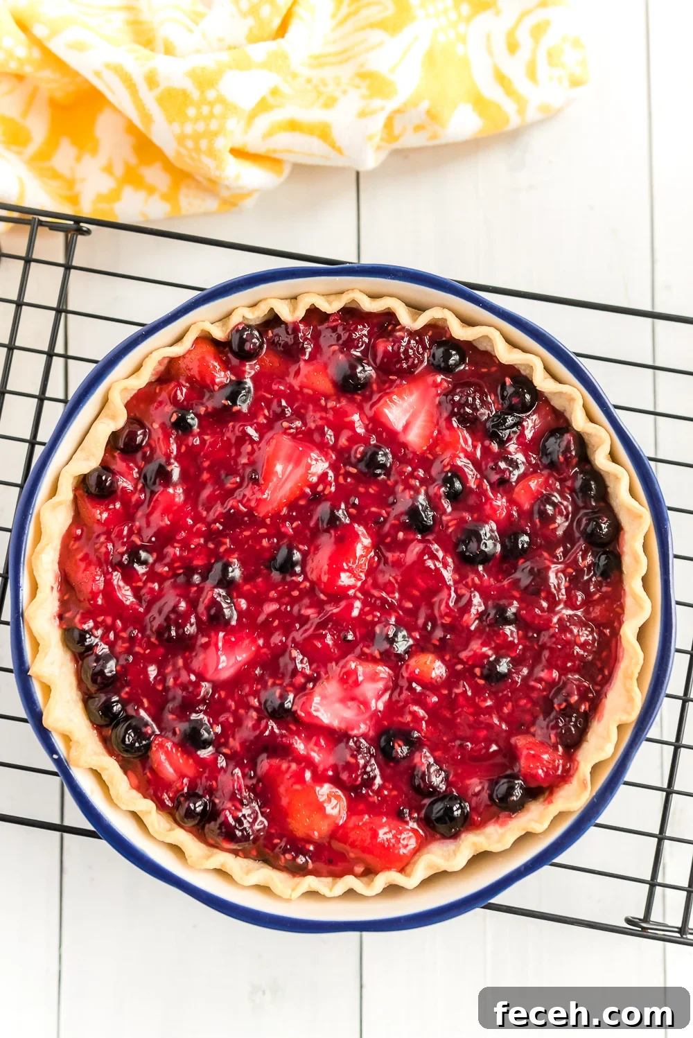 Mixed Berry Pie on black cooling rack on white wood with yellow napkin.