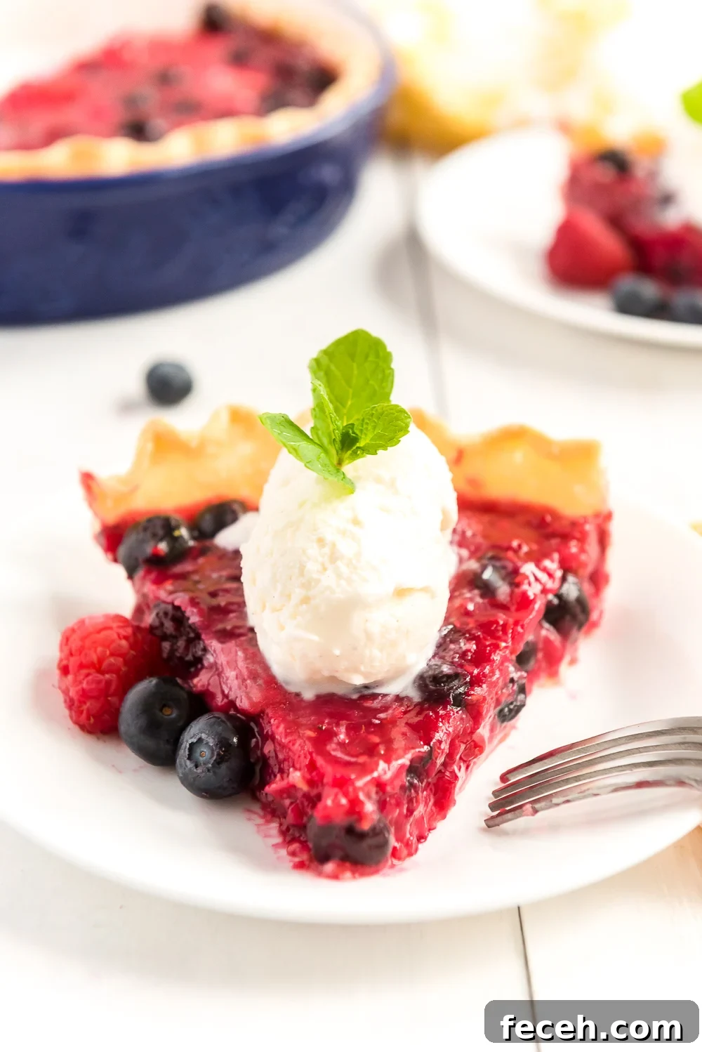 Straight on photo of a slice of Mixed Berry Pie pointed towards the camera with scoops of vanilla ice cream on top and fresh berries on the side.