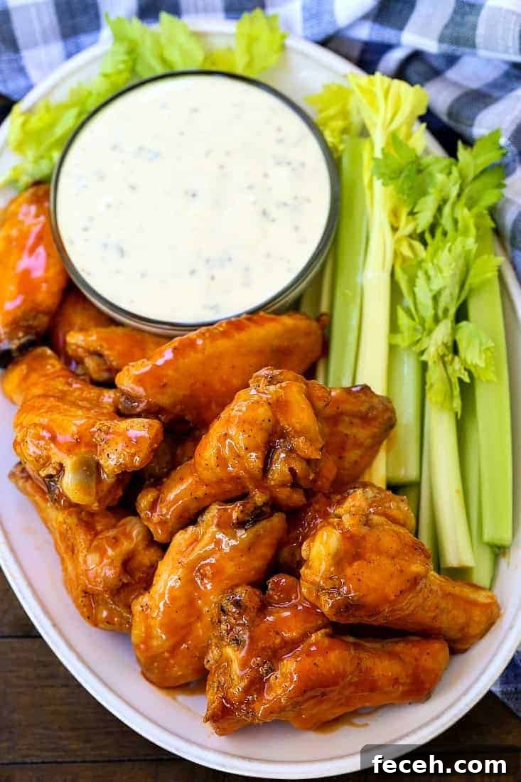 These Crispy Buffalo Chicken Wings are SO addicting and fall off the bone tender! A few tips make them as crispy as if you fried them! buffalo chicken wings on a platter with celery sticks and ranch