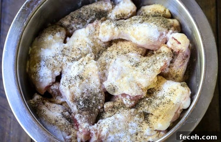 These Crispy Buffalo Chicken Wings are SO addicting and fall off the bone tender! A few tips make them as crispy as if you fried them! chicken wings in a bowl with seasonings