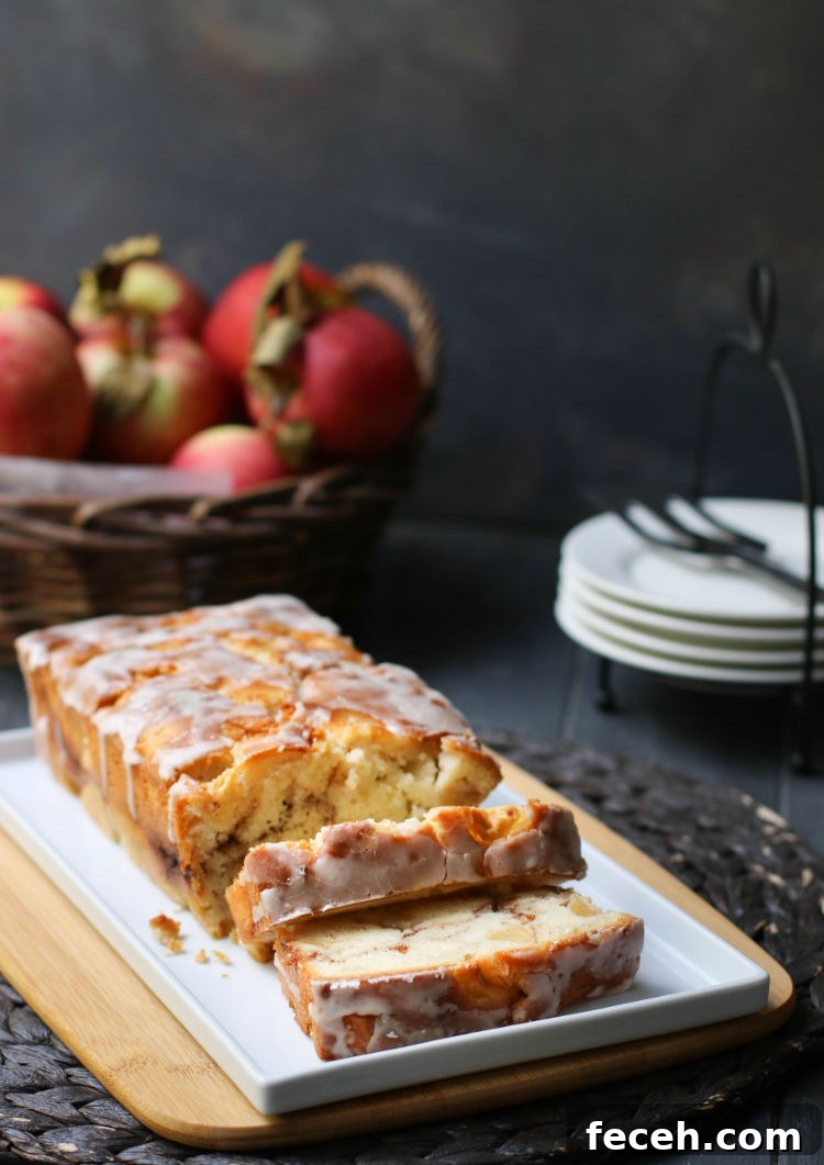 Sliced Apple Fritter Bread on a white plate in front of a basket of apples and a stack of white plates to serve it on.