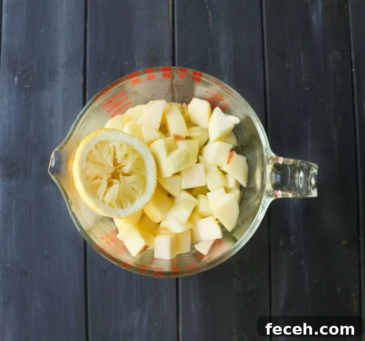 Glass measuring cup filled with peeled apple chunks and a lemon half that's been squeezed