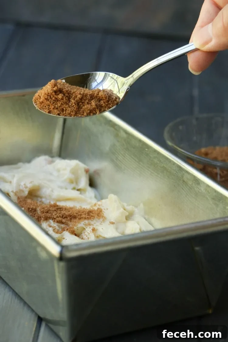 A spoonful of cinnamon sugar being sprinkled on top of Apple Fritter Batter in a loaf pan