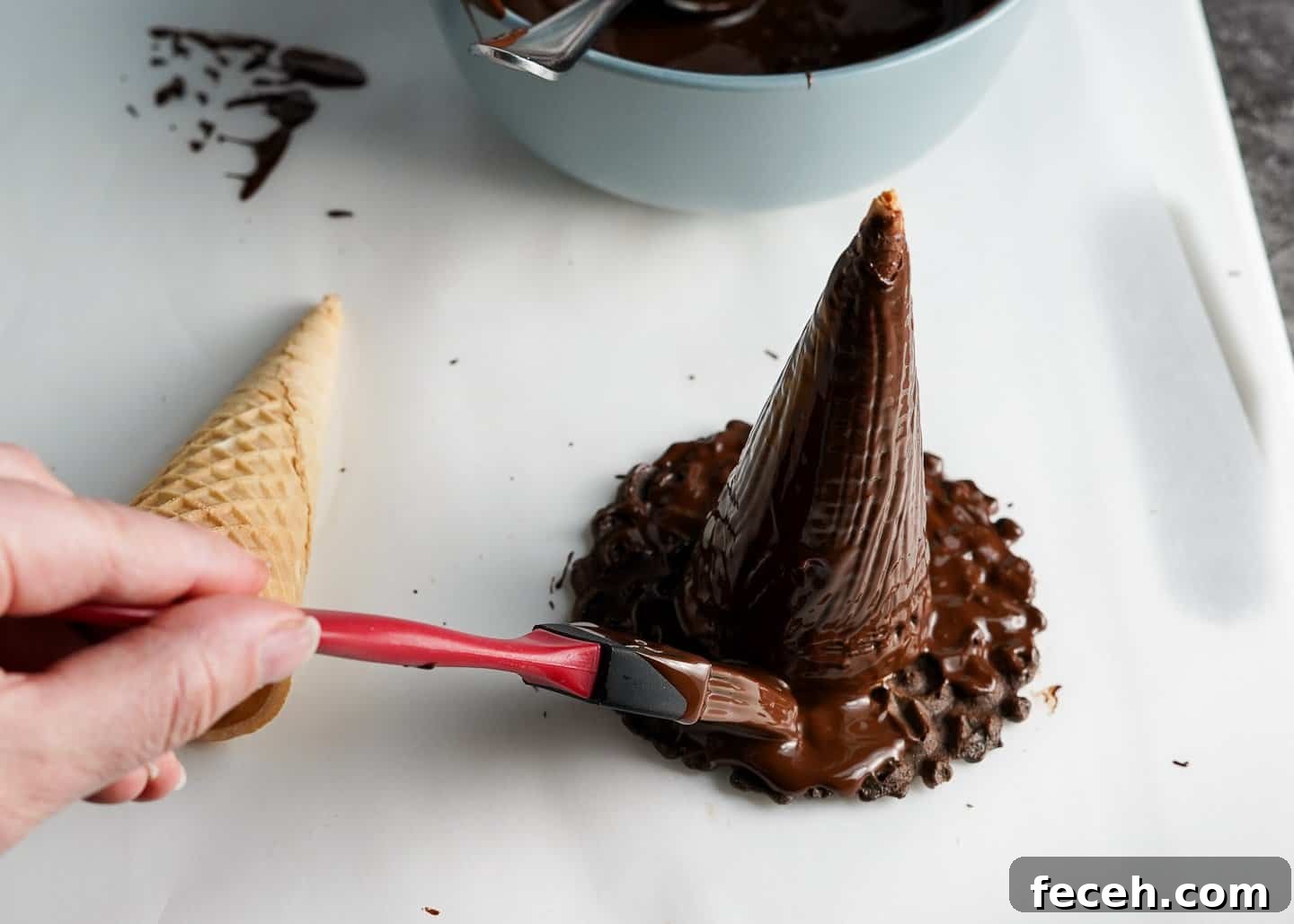 Painting chocolate on brim of witch hat made of ice cream cone and pizelle cookie