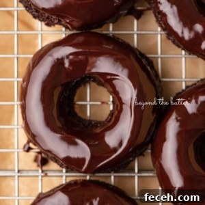 Homemade Baked Chocolate Donuts Recipe — Soft & Fudgy Treats 13 Homemade baked chocolate donuts topped with chocolate ganache glaze on a wire cooling rack.