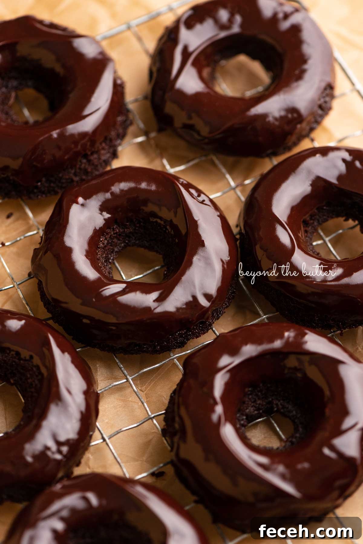 Homemade Baked Chocolate Donuts Recipe — Soft & Fudgy Treats 4 Homemade baked chocolate donuts topped with chocolate ganache on a wire cooling rack | © Beyond the Butter®