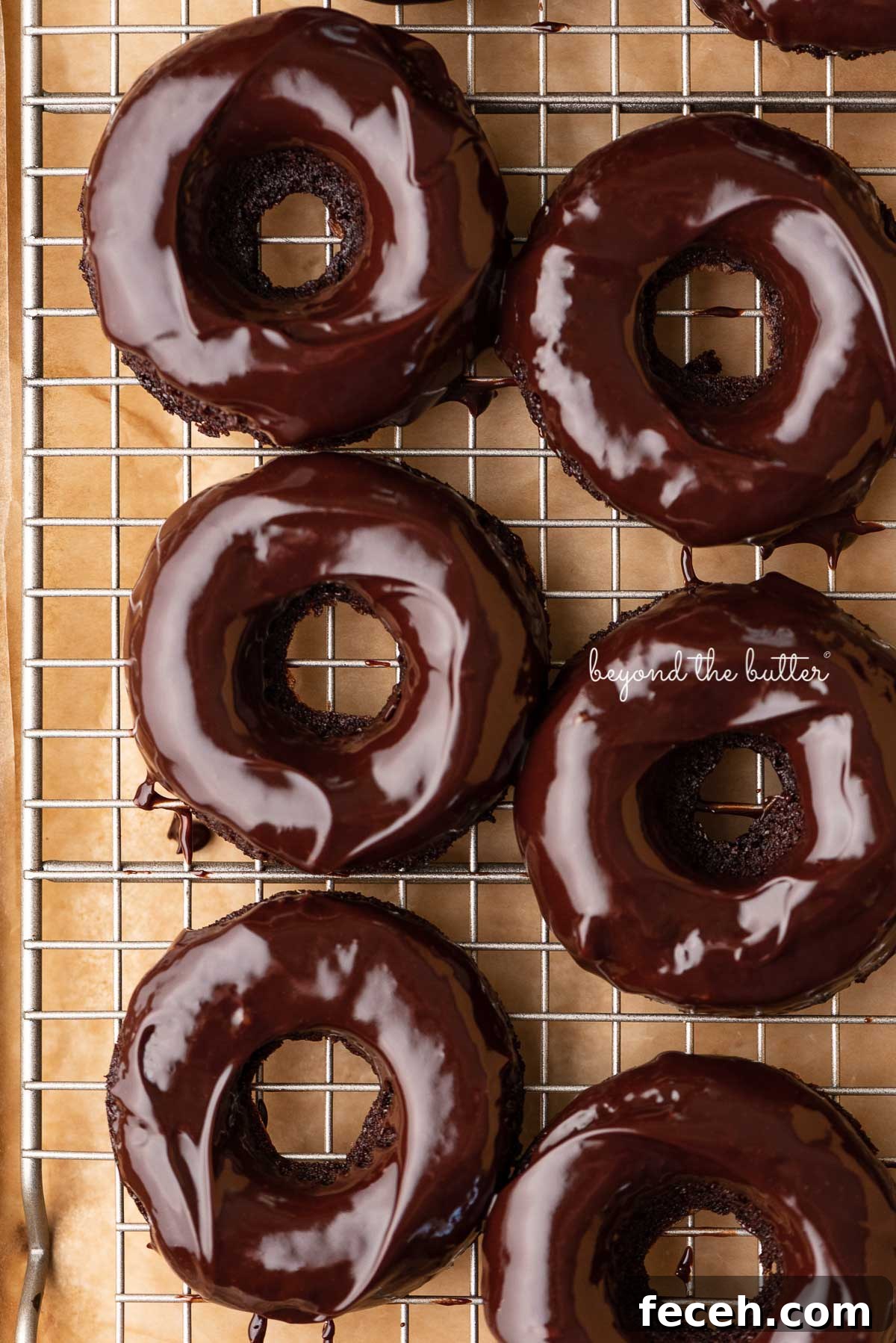 Homemade Baked Chocolate Donuts Recipe — Soft & Fudgy Treats 6 Homemade baked chocolate donuts topped with chocolate ganache on a wire cooling rack | © Beyond the Butter®