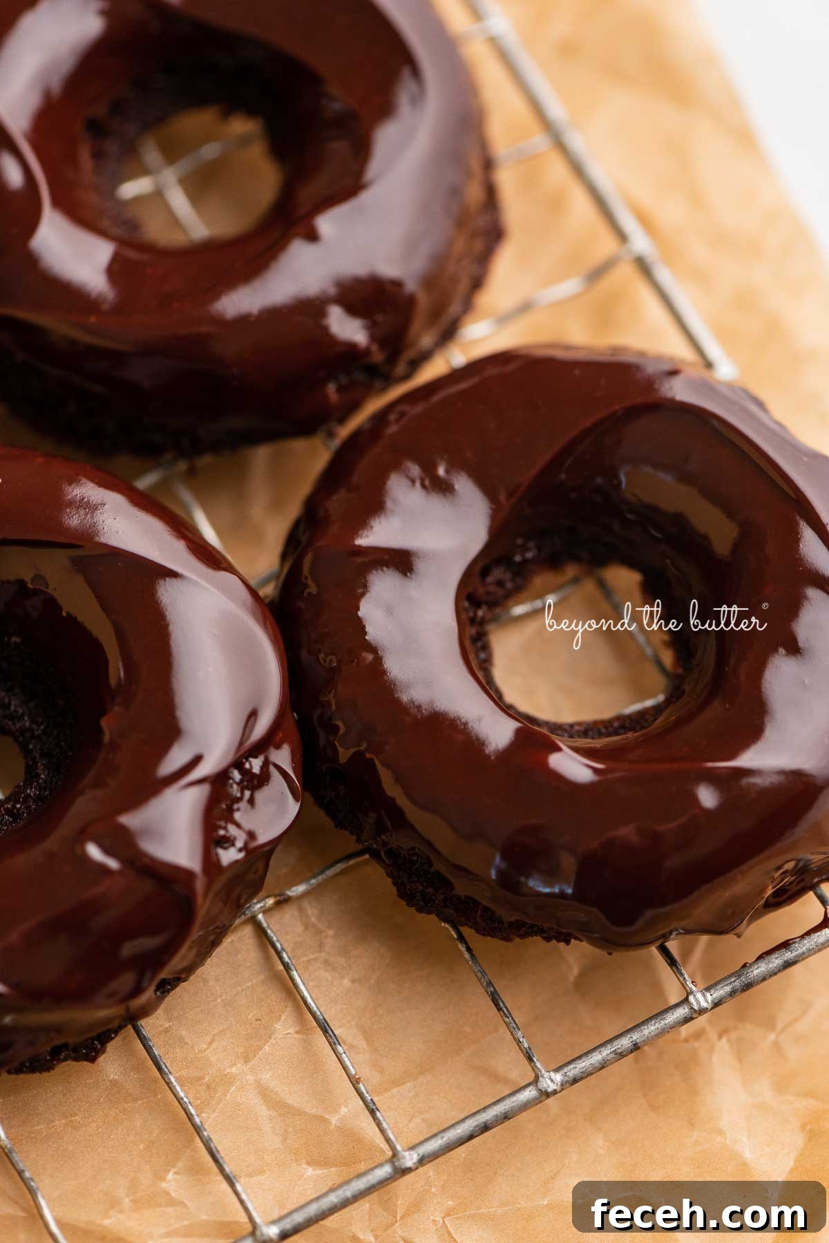 Homemade Baked Chocolate Donuts Recipe — Soft & Fudgy Treats 7 Homemade baked chocolate donuts topped with chocolate ganache on a wire cooling rack | © Beyond the Butter®