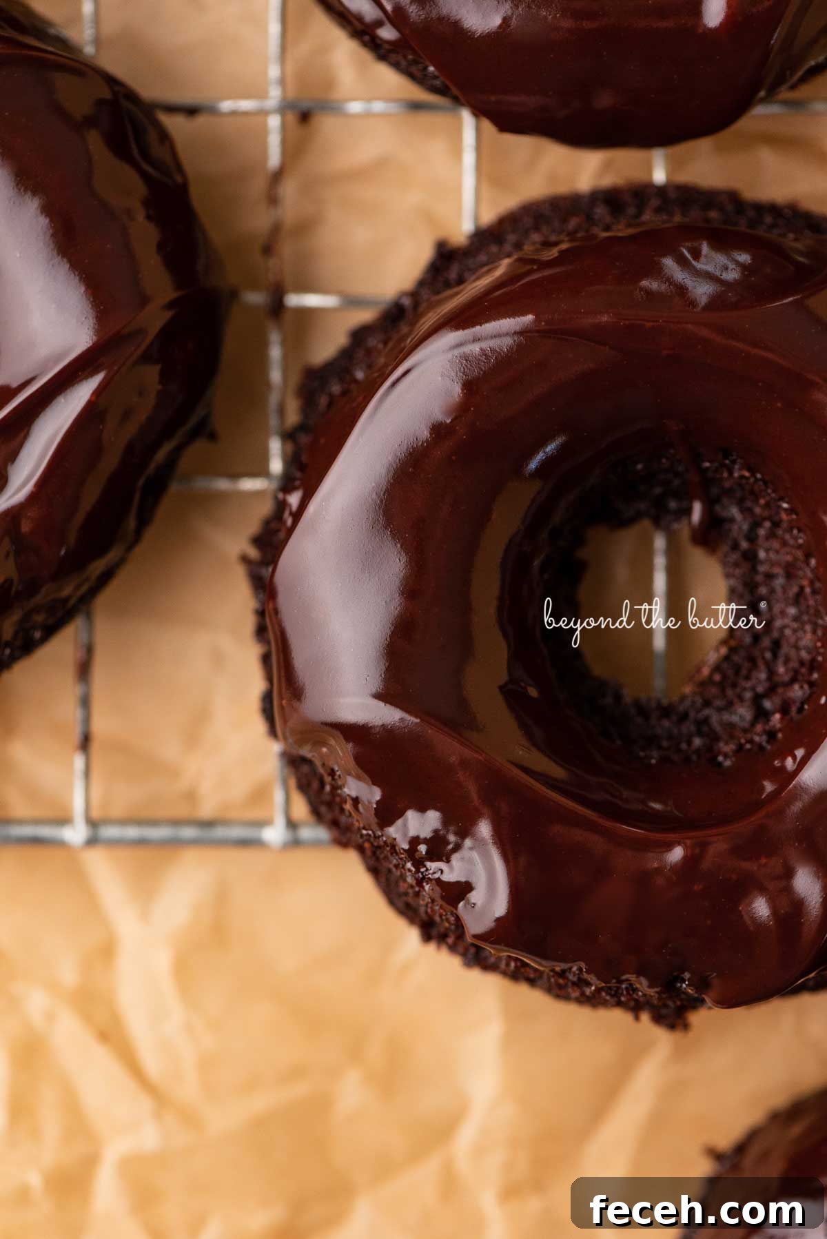 Homemade Baked Chocolate Donuts Recipe — Soft & Fudgy Treats 8 Close up of homemade baked chocolate donuts topped with chocolate ganache on a wire cooling rack | © Beyond the Butter®