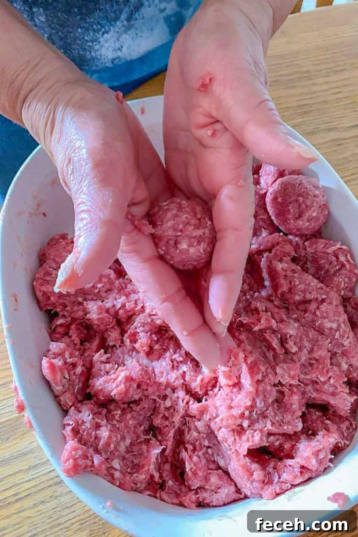 Bowl of raw ground beef and hands forming meatballs