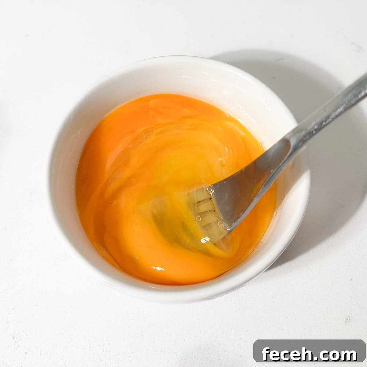 Whisking eggs in a small white bowl with a fork.