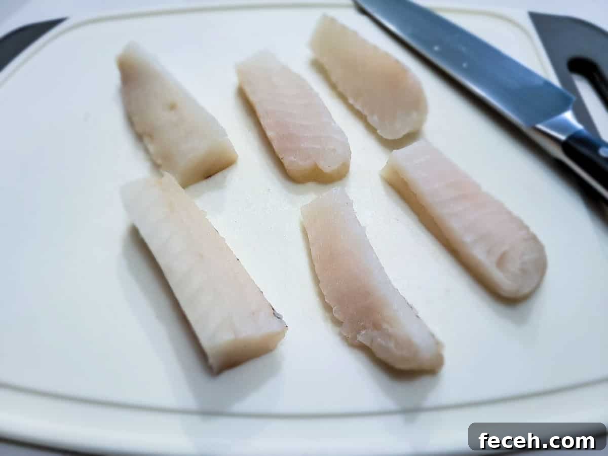 6 strips of cod on a cutting board.