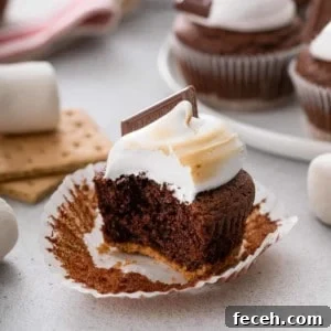 S'mores Cupcakes Recipe: Gooey Campfire Chocolate & Toasted Marshmallow 12 Bite taken from an unwrapped s'mores cupcake.
