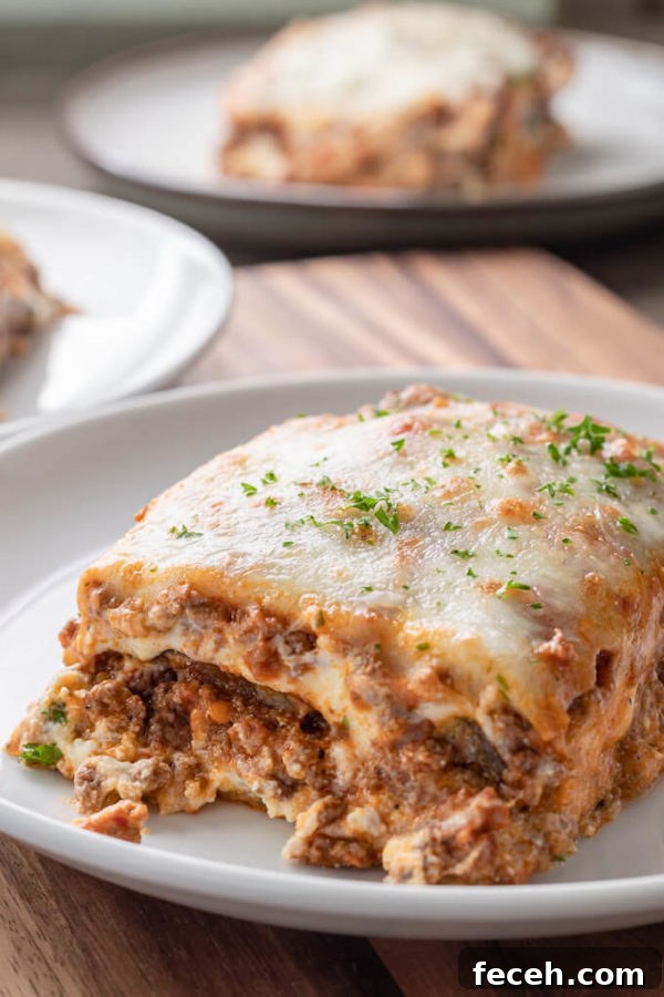 Slice of eggplant lasagna with meat sauce topped with chopped parsley on a white plate.