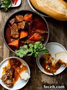 15 Global Soups and Hearty Stews to Warm Any Night 14 Bo Kho stew in a bowl with beef and carrot chunks surrounded with plates and bread.
