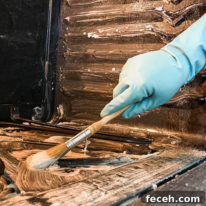 using paintbrush to apply cleaning mixture to bottom of oven