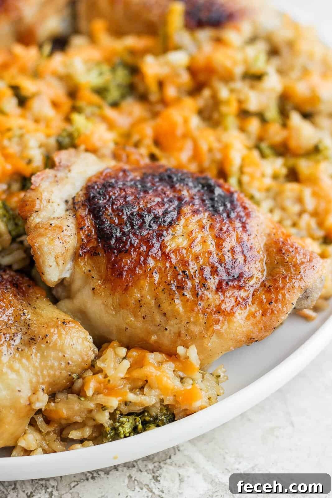 A seared chicken thigh on a white plate with cheesy rice and broccoli.