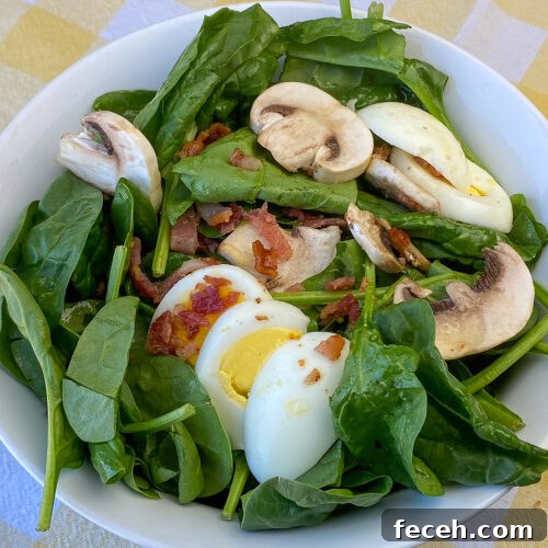 Spinach Salad with Bacon, Mushrooms, and Warm Balsamic Dressing 10 Overhead view of mushroom, spinach, bacon and egg salad in white bowl on a yellow plaid napkin