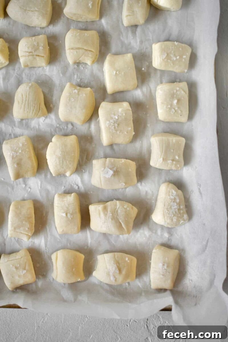 Soft Homemade Pretzel Bites Recipe for Perfect Party Snacks 12 Dipped dough lined up on a sheet pan and some of the pretzel bites dusted with flakey salt, before baking.