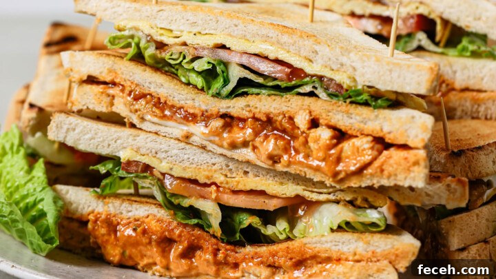 A plate stacked with club sandwiches containing lettuce, tomato, and a saucy filling, each sandwich held together with toothpicks.