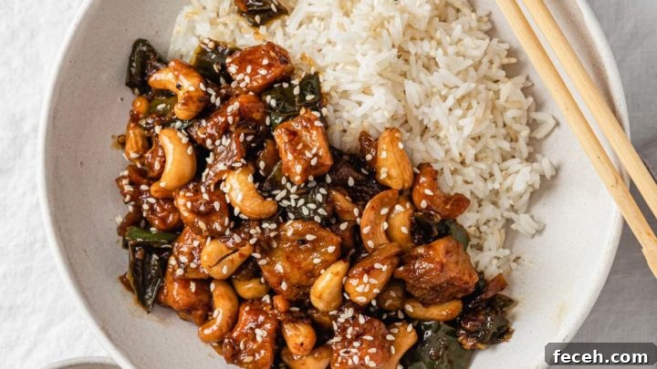 Spicy Cashew Chicken in a bowl with rice with chopsticks and sesame seeds on the side