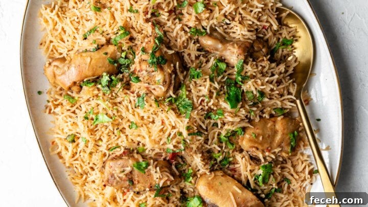 Chicken pulao on a platter with a golden spoon and raita on the side.