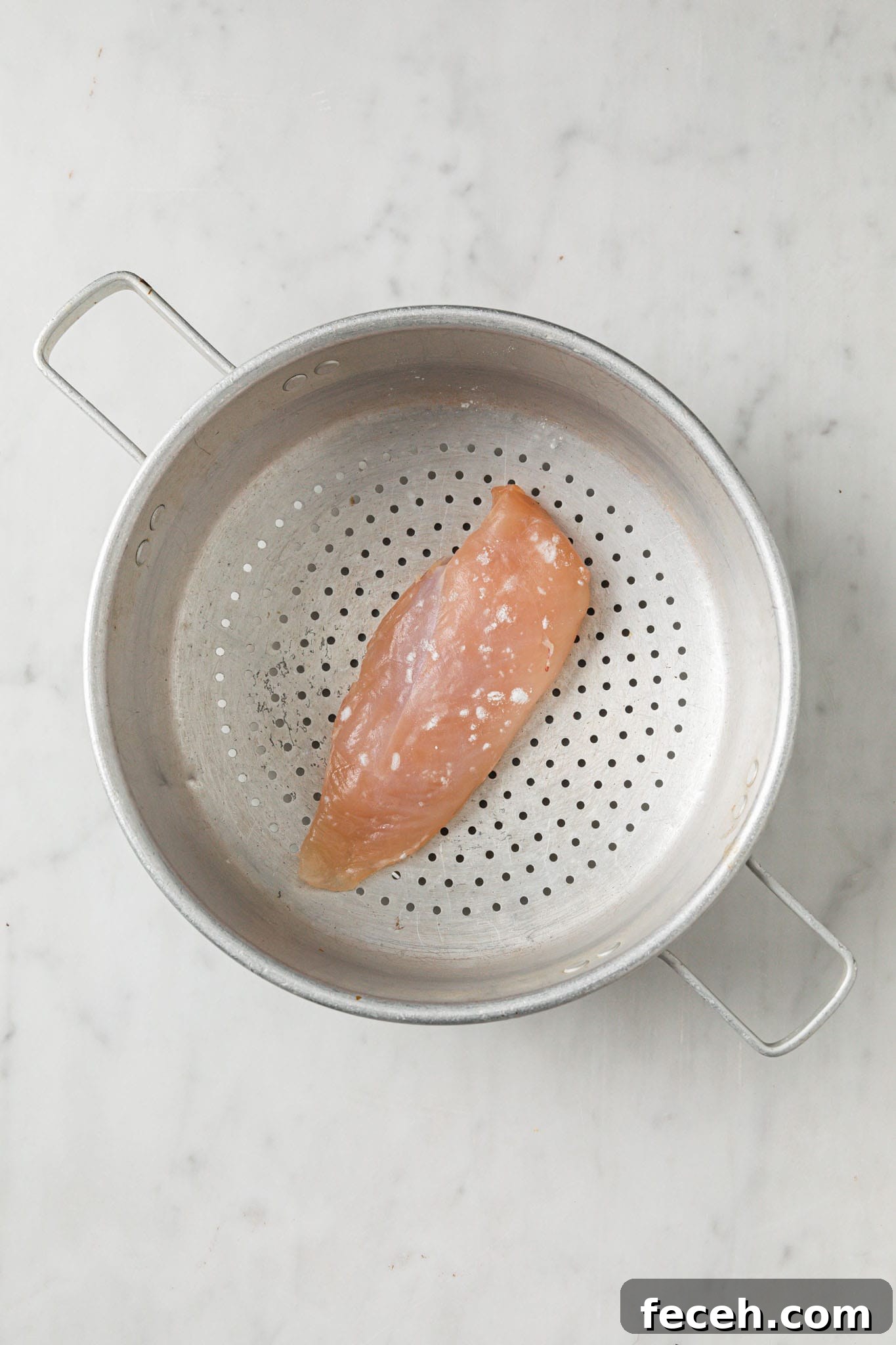 A chicken breast placed inside a colander
