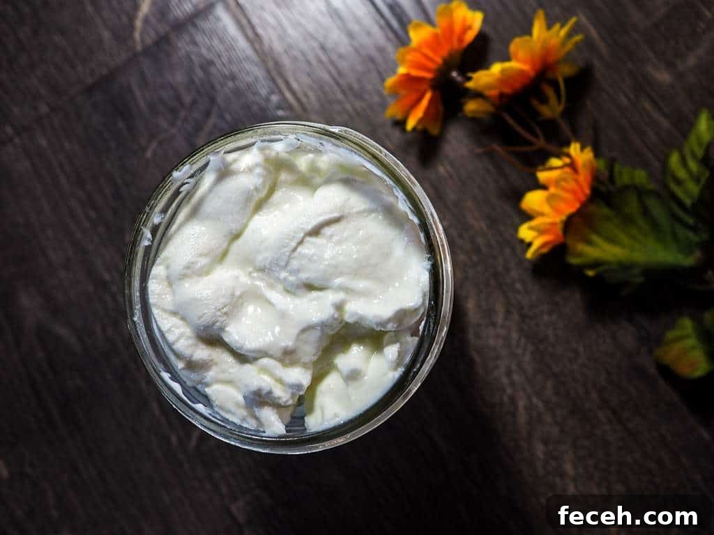 A mason jar full of homemade yogurt and a yellow flower on a gray wood background.