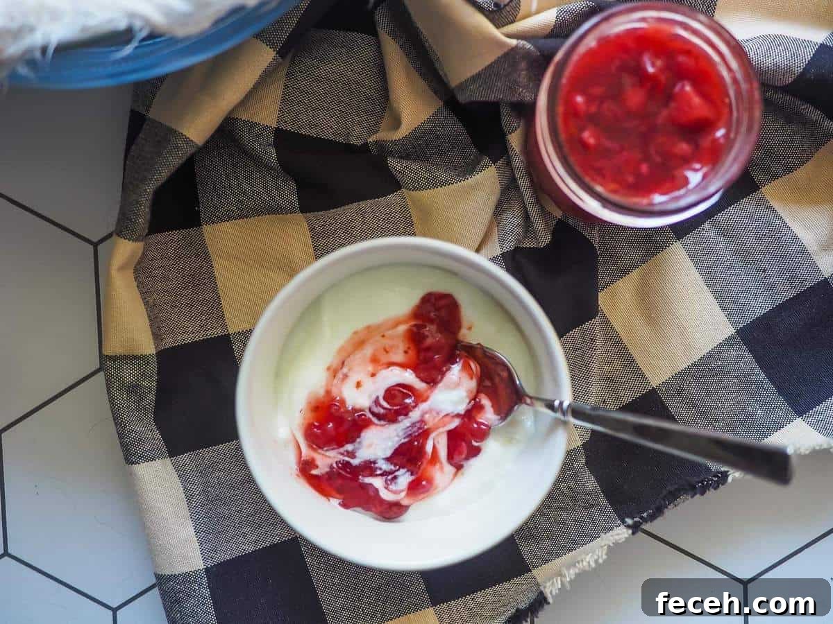 A white bowl of yogurt with paleo strawberry jam on top and a jar of strawberry jam on the side.