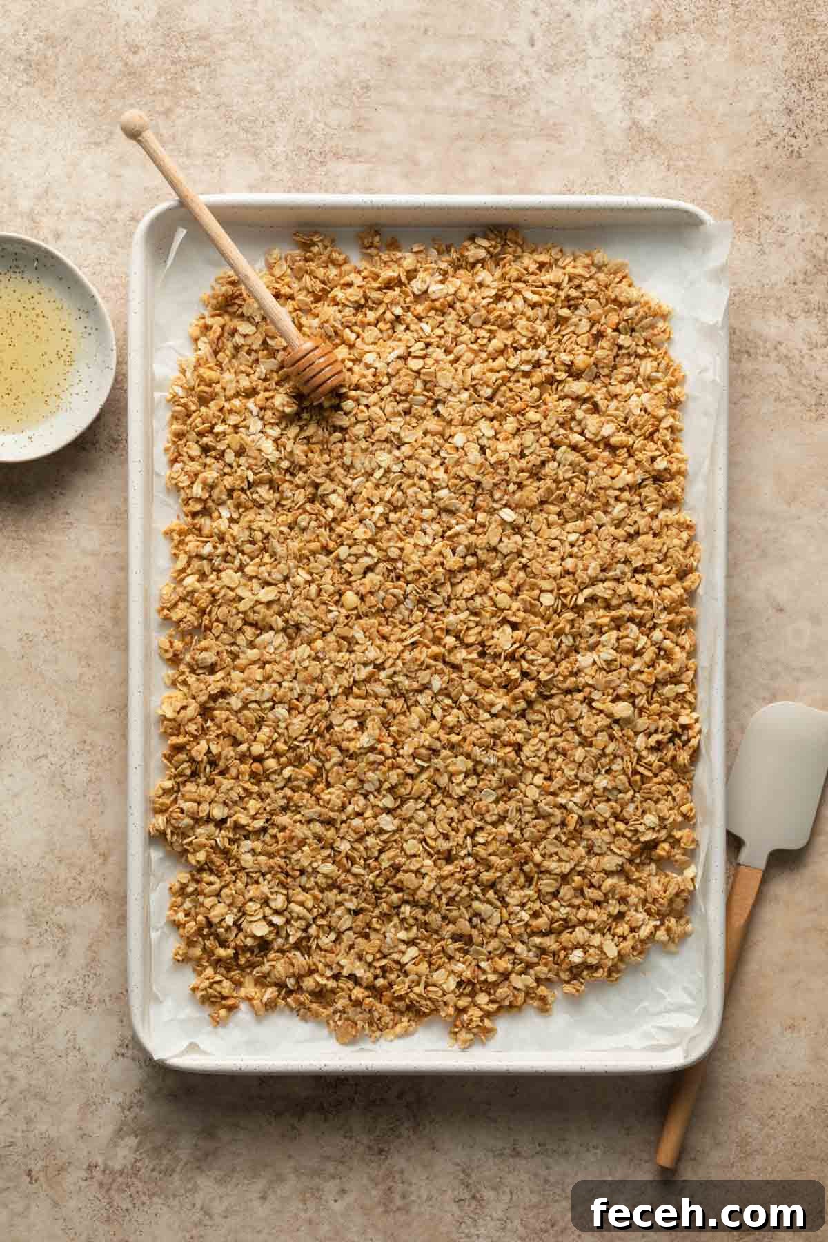 Granola mixture spread out on a white baking sheet.