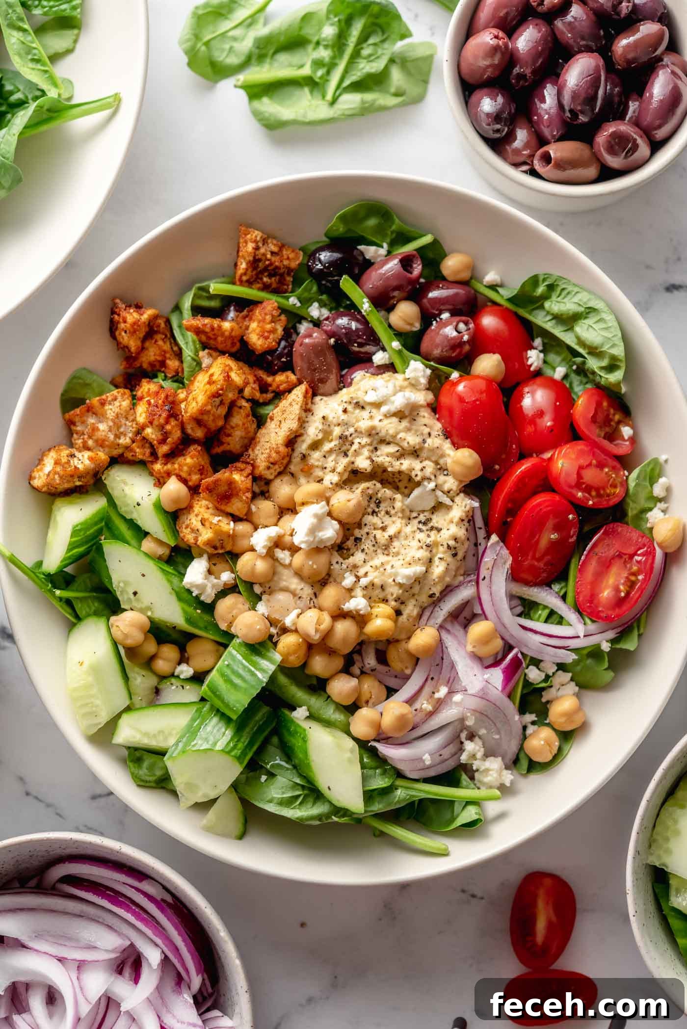 Healthy bowl with spinach, hummus, tomato, red onion, cucumber and olives.