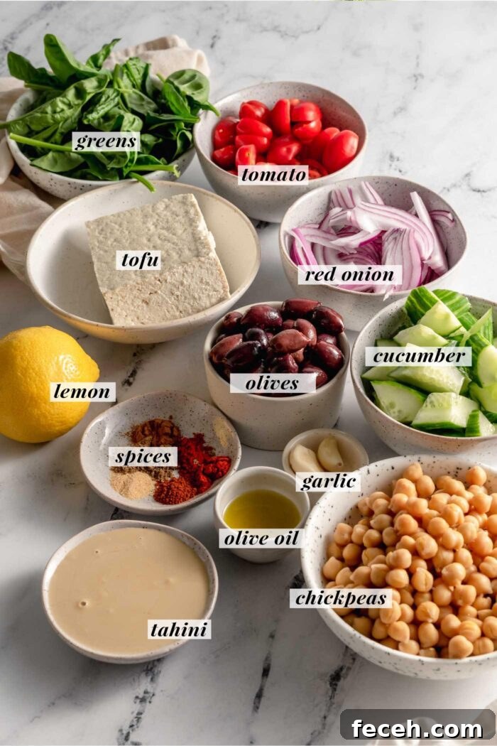 All the ingredient gathered for making a vegan hummus buddha bowl with tofu, homemade hummus and fresh vegetables. Each ingredient is labelled with a text description. The list can be found in the corresponding blog post.