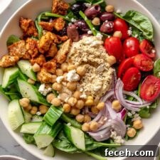 Overhead view of a colourful healthy bowl with spinach, hummus, tomato, red onion, cucumber and olives.