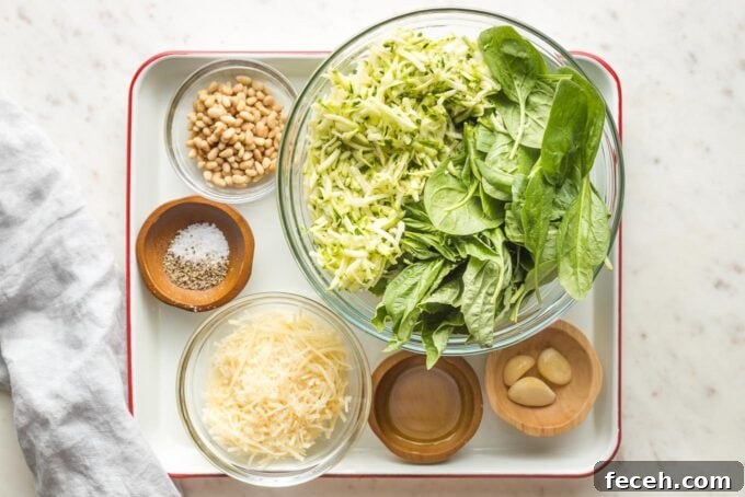Prep bowls containing grated zucchini, spinach and basil leaves, Parmesan cheese, garlic, pine nuts, olive oil, salt and pepper.