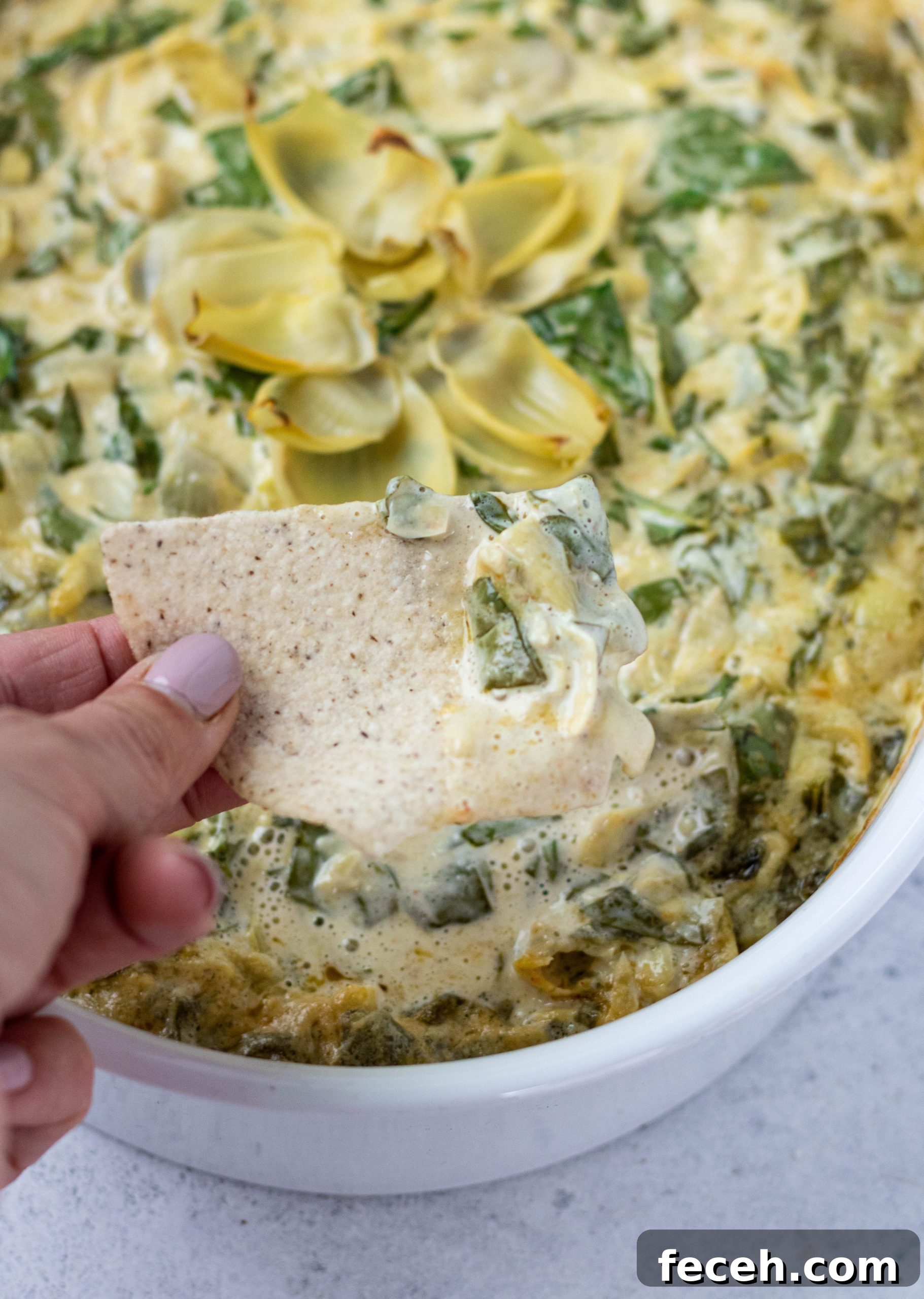 a hand with a chip scooping up dairy free spinach artichoke dip
