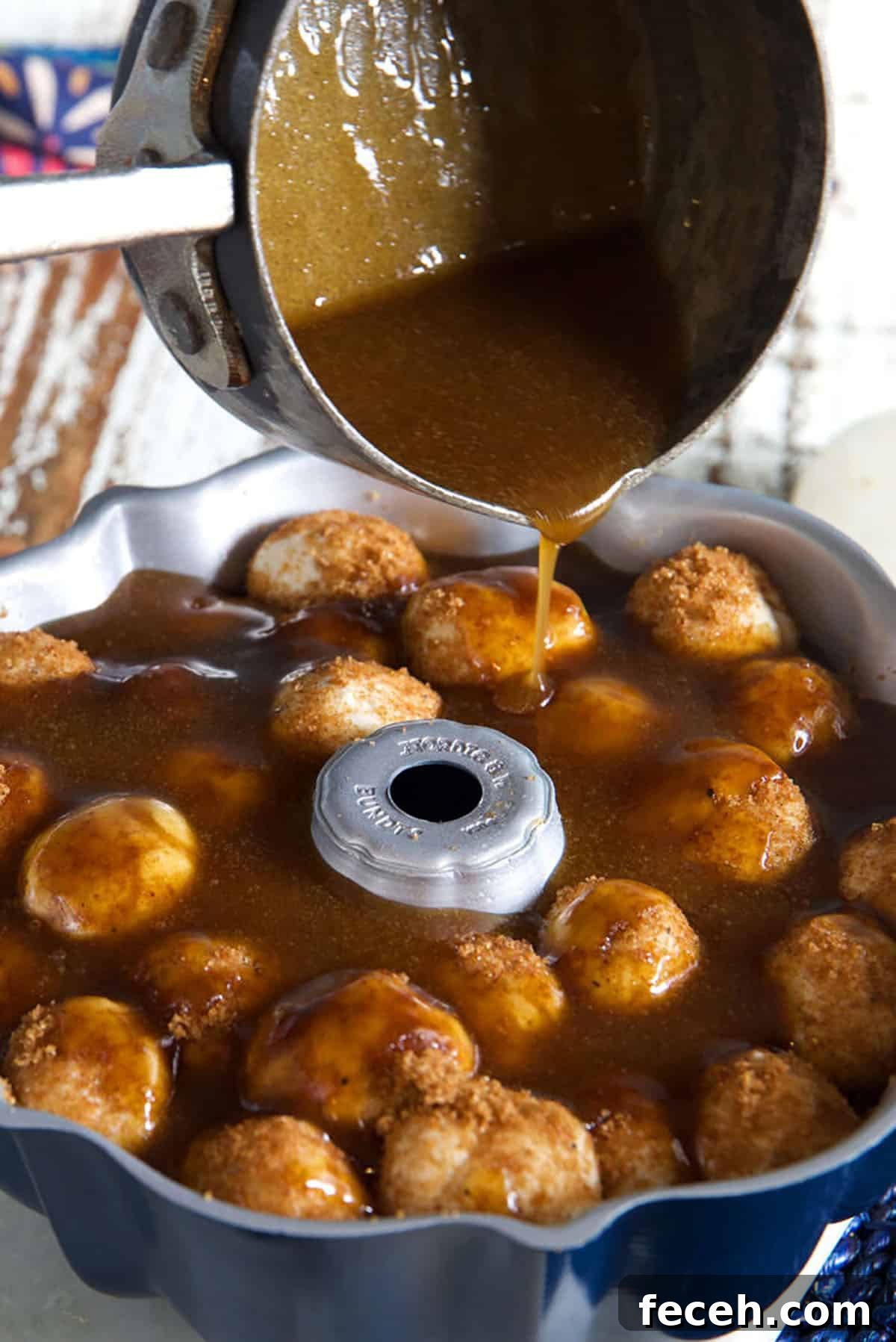 Sauce is being poured from a pot onto a ring of monkey bread.