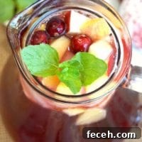 Cranberry Sangria Recipe: Festive Cocktail for Holiday Gatherings 2 A glass pitcher of sparkling cranberry sangria brimming with apple cubes, fresh cranberries, and a mint garnish.