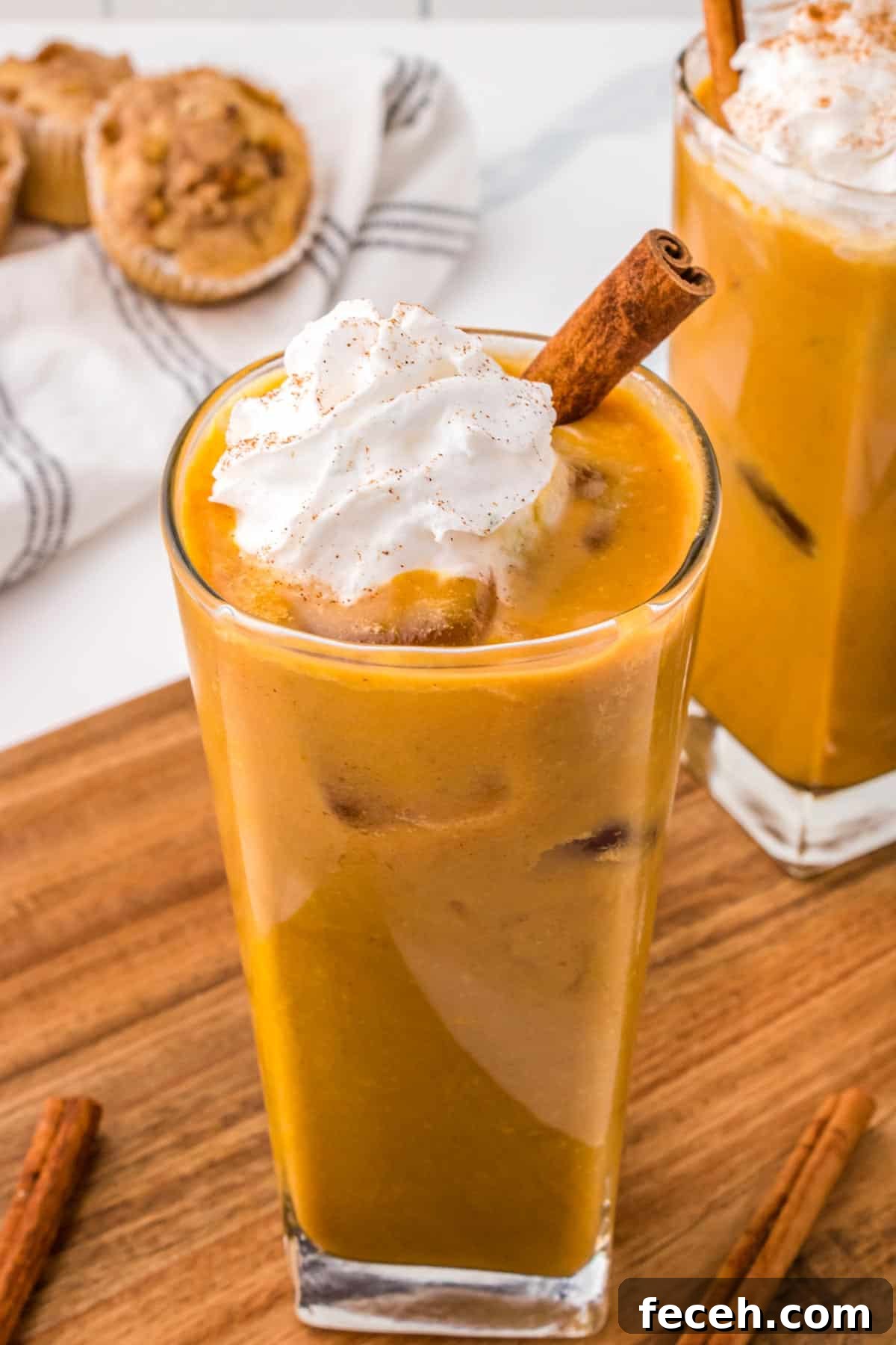 Pumpkin spiced iced latte in a glass topped with whipped cream and a cinnamon stick.