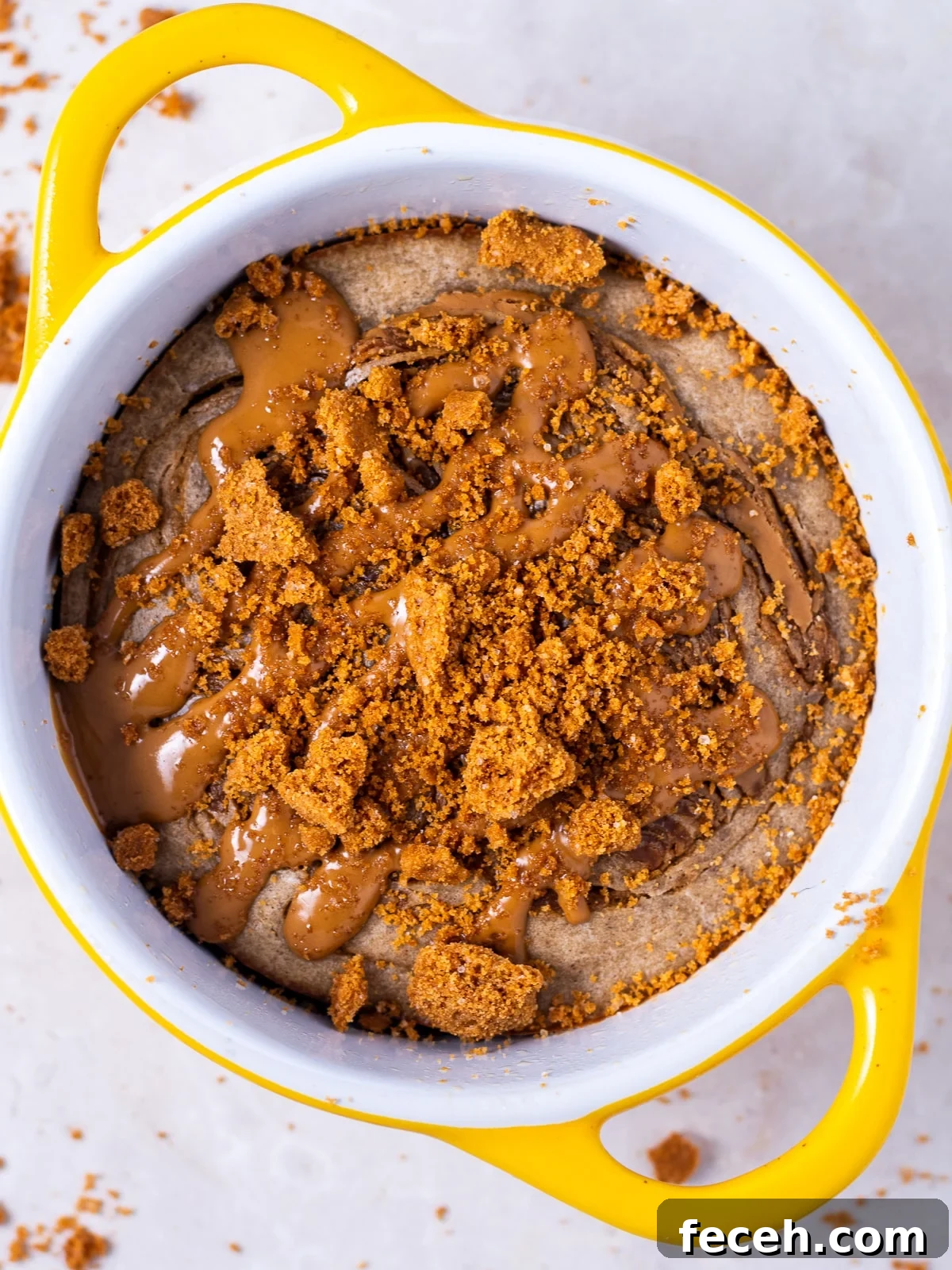 yellow ramekin filled with baked oatmeal and topped with biscoff spread and biscoff cookie crumbles
