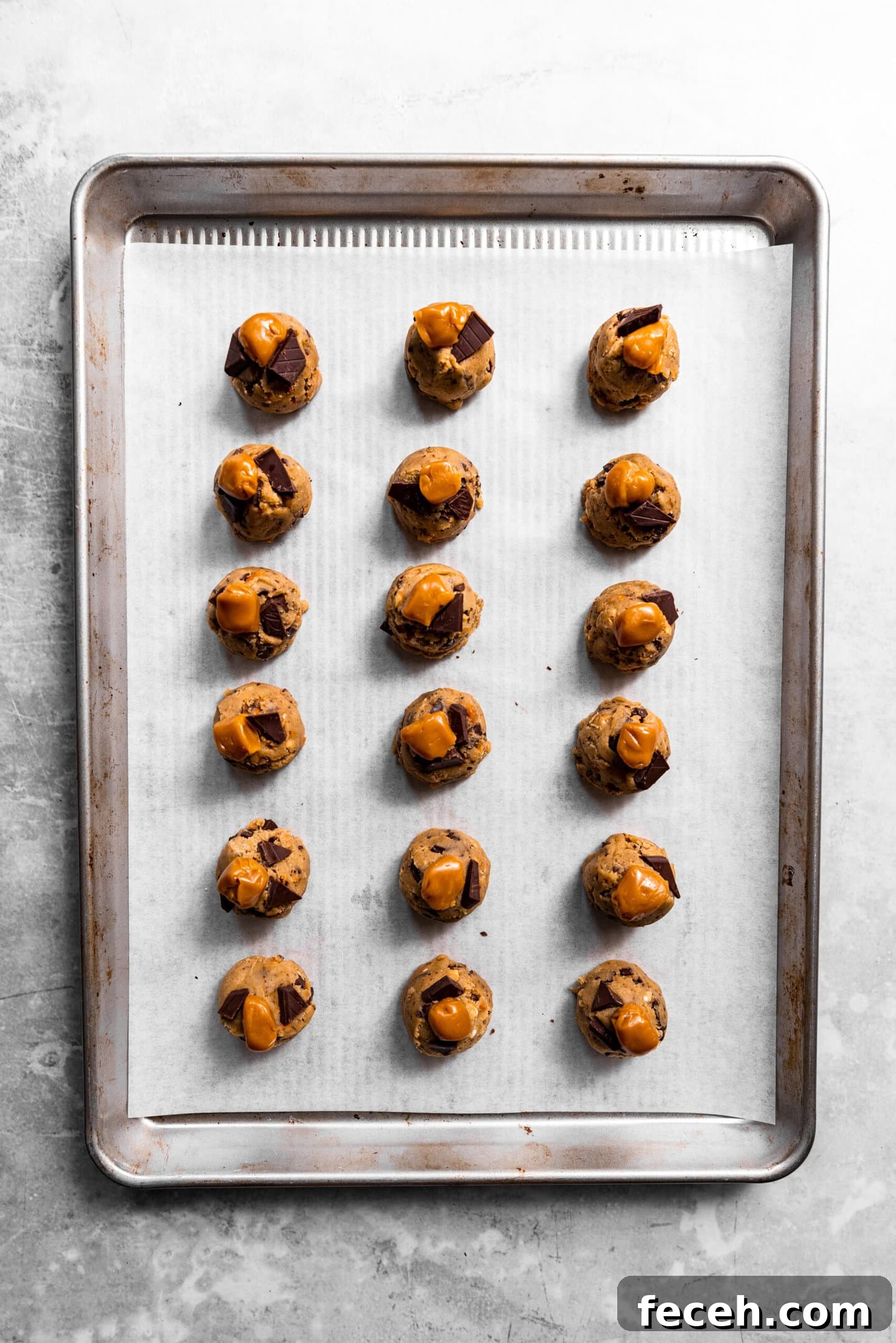 Cookie dough on baking sheet with caramel and chocolate chunks on top.